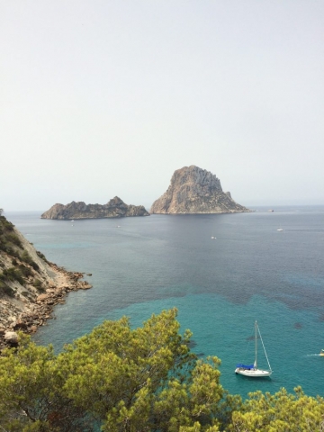 Blick auf Es Vedrá mit Segelboot und Bäumen
